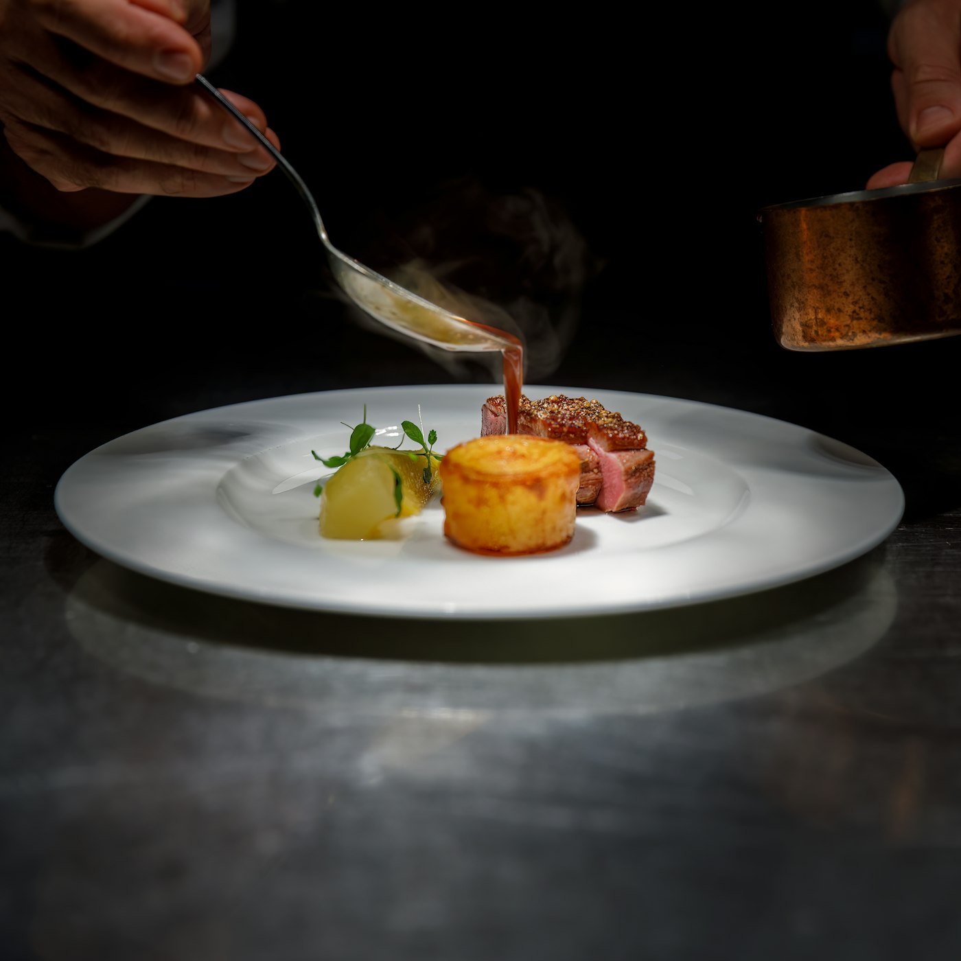 Chef spooning sauce over a plated dish