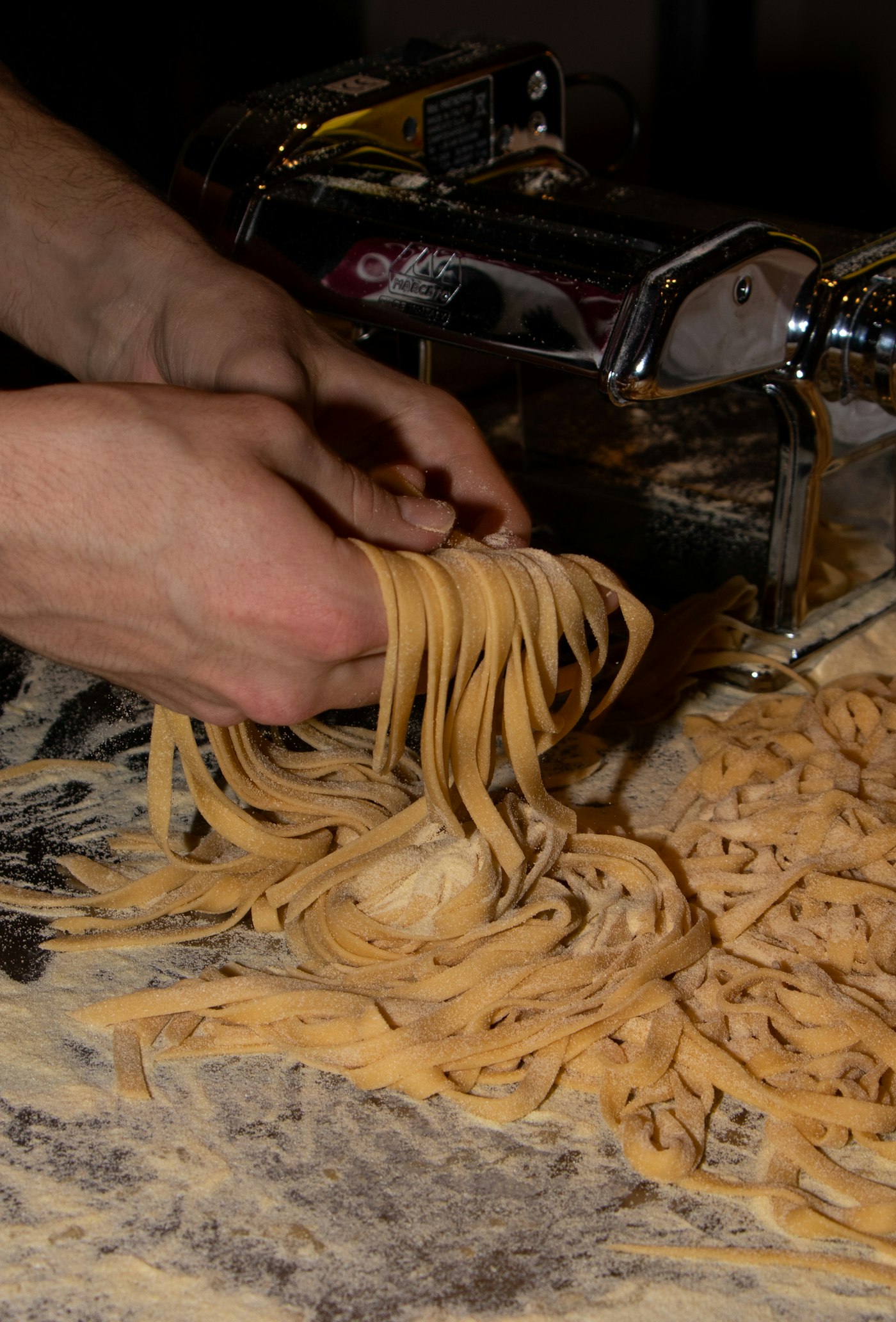 Chef's hands feeding fresh pasta through a pasta machine