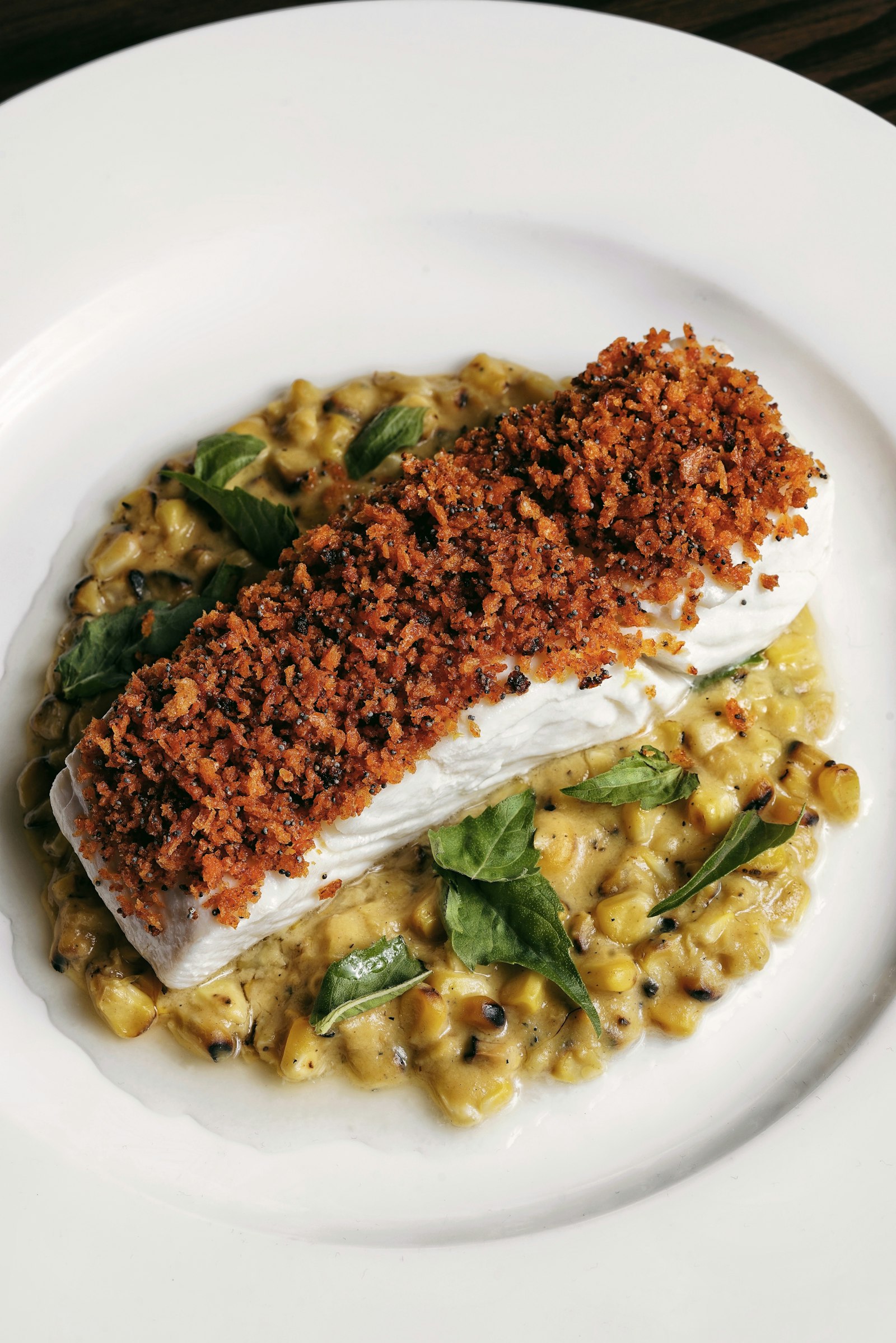 Fish fillet with herb crust on vegetables in a white plate