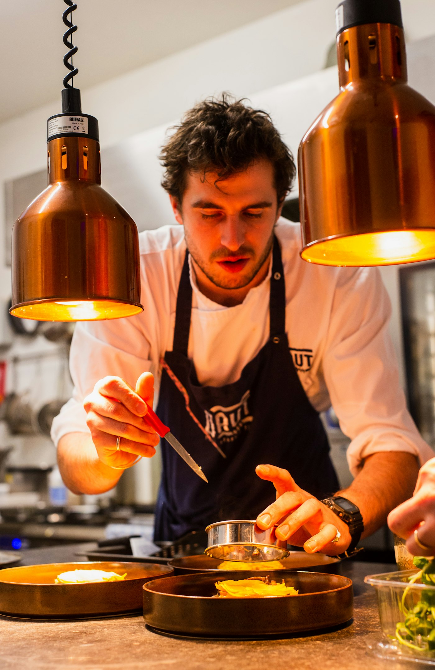 Chef in an apron preparing a dish under warm kitchen lights